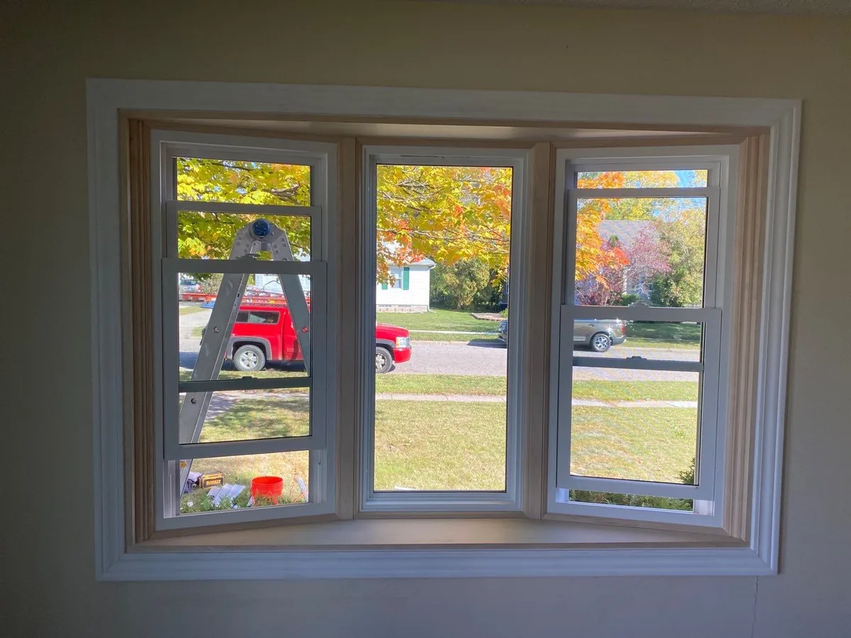 Wide interior perspective looking out through a massive three-panel bay window with oak casing
