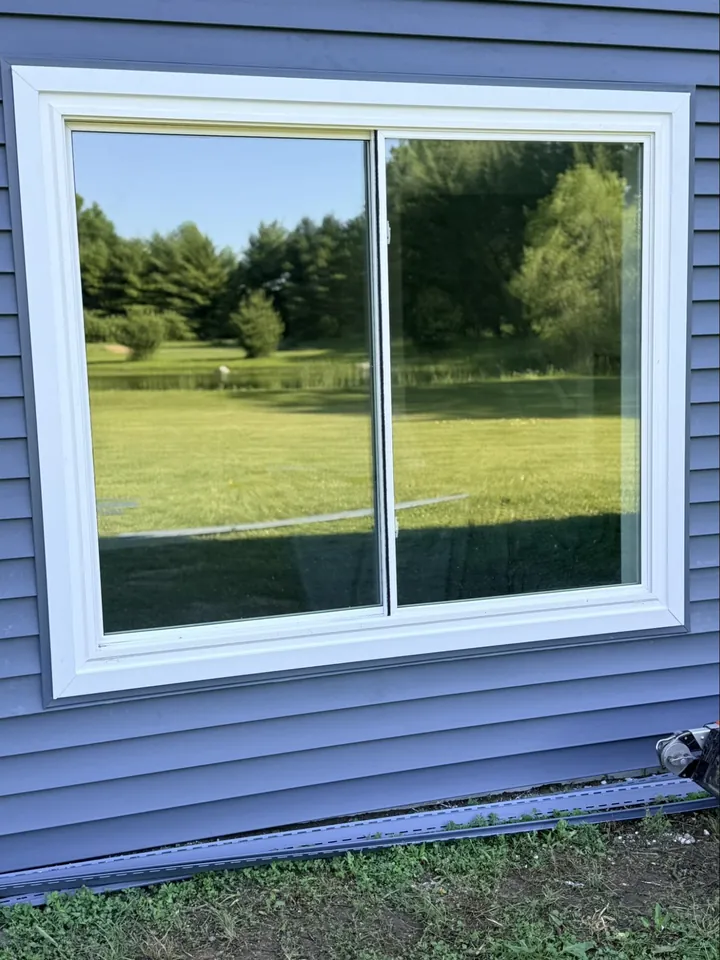 Close-up white horizontal slider on blue vinyl siding with backyard landscape reflection